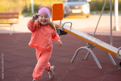 Canvastavla Little girl running happily on playground with toy in hand near seesaw