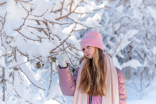 Fotografie Little girl touching snow-covered tree branches in a winter forest