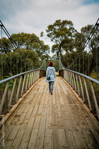 Rear view of a woman walking across a timber suspension bridge surrounded by native woodland, Donald, Victoria, Australia