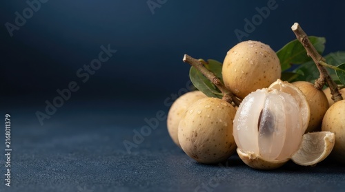 Fresh organic longan fruit cluster with translucent juicy flesh and green leaves isolated on a dark blue textured background for culinary usage