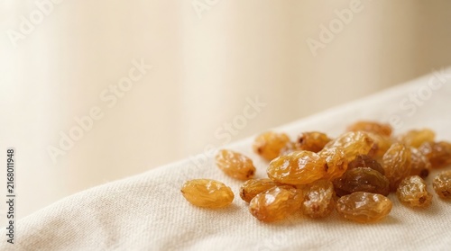 A close-up horizontal shot of high-quality sun-dried golden raisins arranged neatly on a clean beige fabric texture for a natural food photography