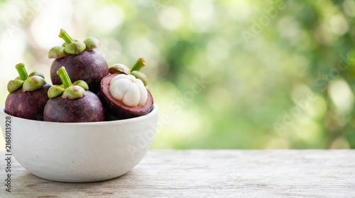 Freshly picked mangosteen fruits arranged in a rustic white bowl placed on a textured wooden table with a soft natural blurred garden background