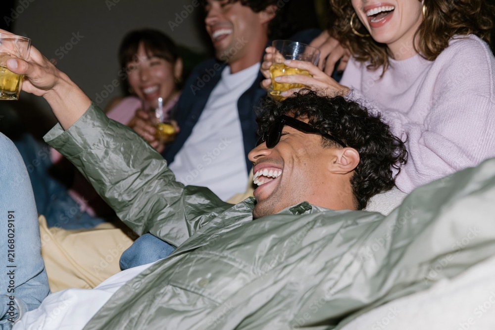 Obraz premium Group of diverse young adults laughing and holding drinks in a natural home setting with harsh flash lighting for social life and wellbeing