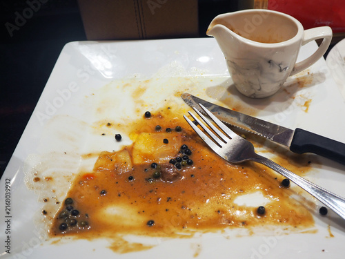 Photography Remnants of a delicious meal on a white plate, with a small pitcher of sauce beside a fork and knife