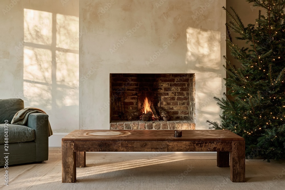 Naklejka premium Empty wooden coffee table with a weathered orange top in a cozy living room with a burning fireplace and Christmas tree, for product mockup and copy space