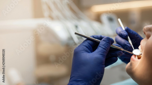 Dentist examining patient tooth with dental mirror and metal instrument during careful oral examination in modern clinic