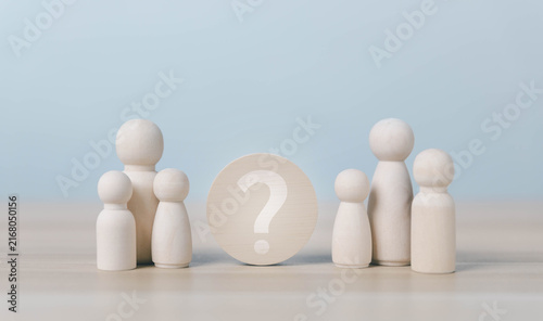 Wooden family figures surround a question mark, symbolizing uncertainty, family decisions, relationship choices, identity, support, communication, and important life choices in a calm setting.