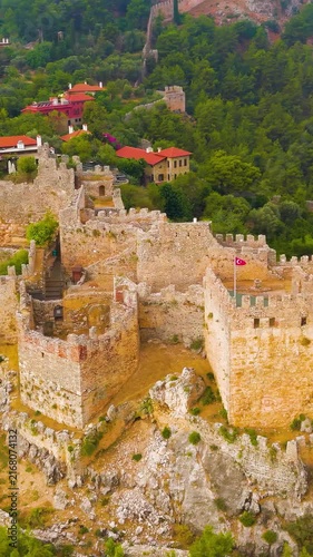 Vertical video. Alanya, Turkey. Ehmedek Castle, three stone towers and defensive walls on a forested hillside, aerial drone view over the Mediterranean coast. Aerial View, Point of interest. Rich col