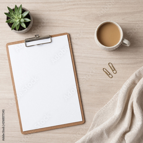 Top view of a clipboard with blank paper, coffee cup, succulent, and fabric on wood