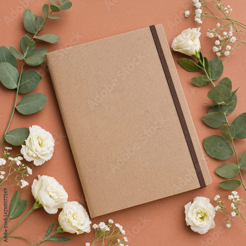 Blank notebook with eucalyptus leaves and white flowers on a terracotta background