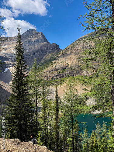Hiker resting on Big Beehive trail above Lake Agnes with mountain peak, Banff