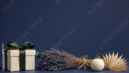 Gift box with green ribbon, lavender bouquet, and christmas ornament on blue background
