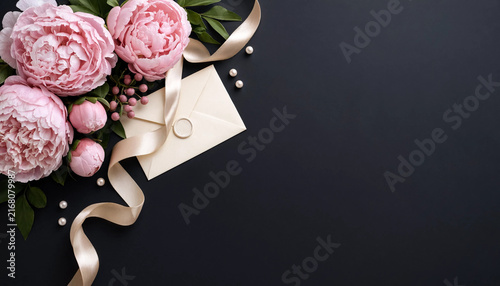 Beautiful pink peony flowers with a cream envelope and ribbon on a dark background