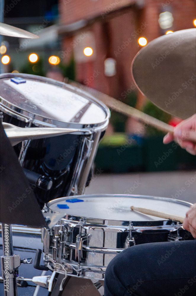 Fototapeta premium Musician performing on drums at an outdoor concert with dynamic hands, sticks and cymbals. Drummer hands striking cymbals and drums during a lively open-air summer music performance.