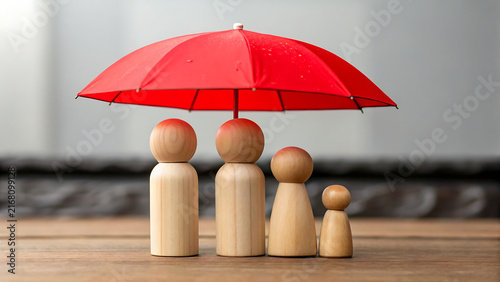 Four wooden figurines sharing a red umbrella on a wooden surface in soft light