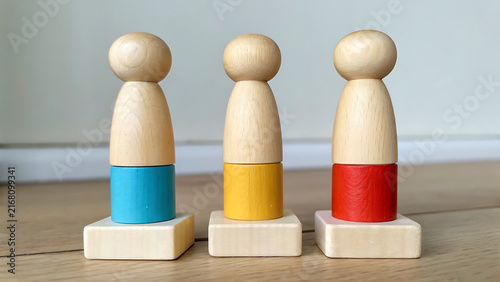 Three minimalist wooden peg dolls with colorful painted sections on neutral background