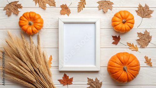 Empty white picture frame with autumn pumpkins, leaves, and wheat on rustic wooden table