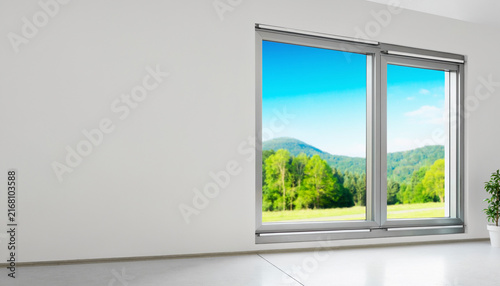 Modern interior room with a large window overlooking a beautiful green landscape and blue sky.