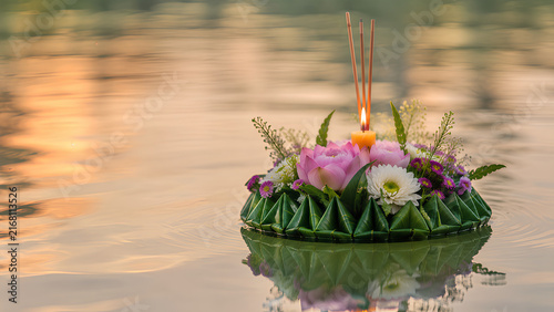 Beautiful traditional Krathong made of banana leaves and lotus flowers with lit candle floating on the river at sunset during Loy Krathong festival