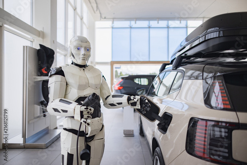 Obraz na płótnie A humanoid robot is shown charging an electric vehicle in a modern showroom, symbolizing future automotive technology and automation