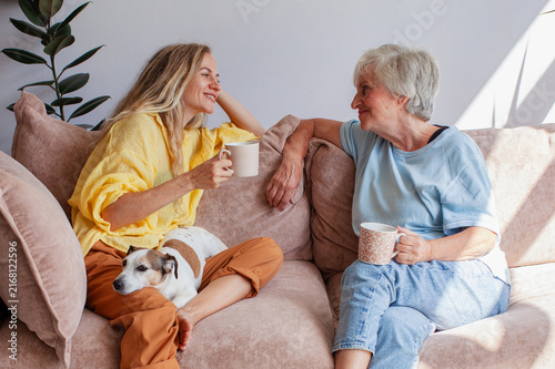 Foto Young woman and elderly woman chatting on sofa with dog holding coffee mug