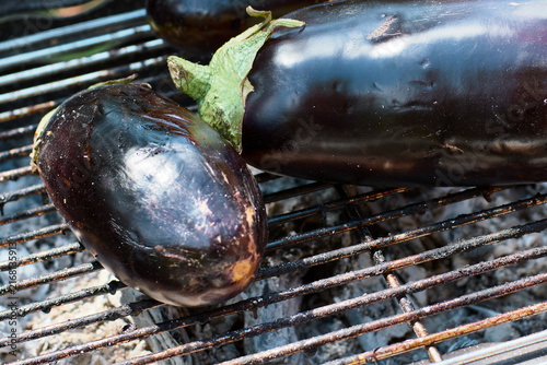 Close-up of fresh whole eggplants grilling on a hot barbecue metal grate