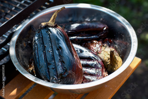 Close-up of roasted eggplants in a stainless steel bowl near a grill