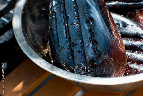 Close-up of a grilled eggplant resting in a metal bowl after cooking outdoors