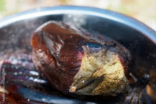 A close-up view of a whole grilled eggplant resting inside a metallic bowl