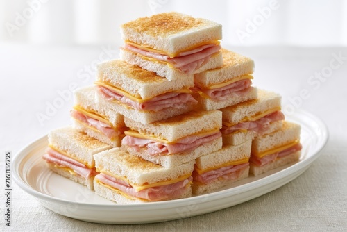 A pyramid of toasted ham and cheese sandwiches served on a white plate. Ideal for party catering and family gatherings.