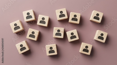 Wooden blocks with a person icon scattered on a dusty pink background, representing teamwork, leadership, or human resources