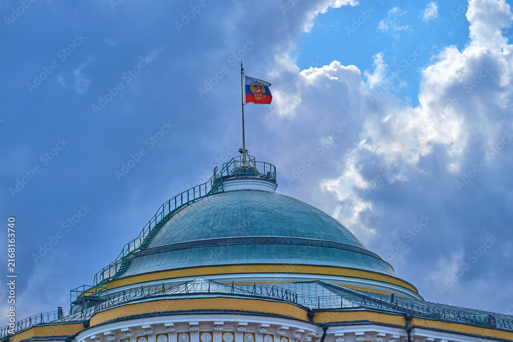 Naklejka premium Senate Palace dome in the Moscow Kremlin with Russian flag against a dramatic blue sky. Historic government architecture and national symbol in Russia.
