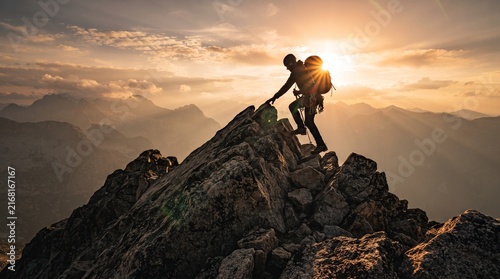 Summit Serenity: A lone hiker, silhouetted against a breathtaking sunset, ascends a rugged mountain peak, embodying the spirit of adventure and accomplishment.