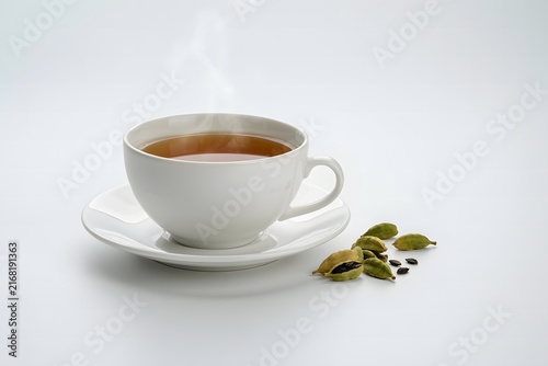 A steaming hot cup of aromatic cardamom tea served on a white saucer with whole green cardamom pods, creating a cozy and relaxing atmosphere for a healthy drink concept.