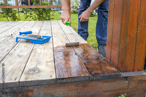 Canvastavla Hand applies wood stain to weathered deck boards using roller