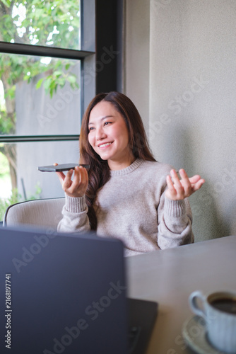 Foto Vertical of a woman holding smart phone and using voice messaging, talking with