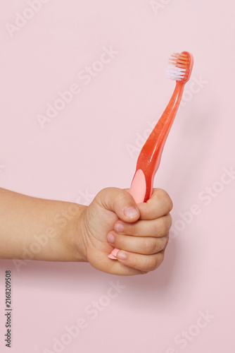 Child hand holding pink toothbrush for oral hygiene