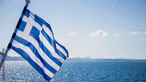 Greek flag billowing from ship above sparkling Aegean Sea water, blue sky, Greece