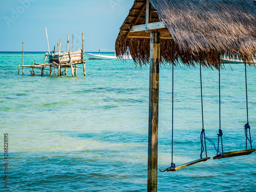 Wooden swings hanging from a thatched roof enjoying the clear blue green ocean water on Barakuda Beach. Creating a relaxing scene highlighting tropical travel and serene island life in Karimunjawa