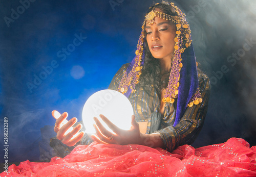 A South Asian woman holding a glowing crystal ball in a mystic setting