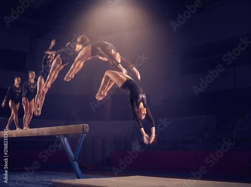 Stroboscopic sequence of a female gymnast performing a flip dismount from a balance beam in a dark arena