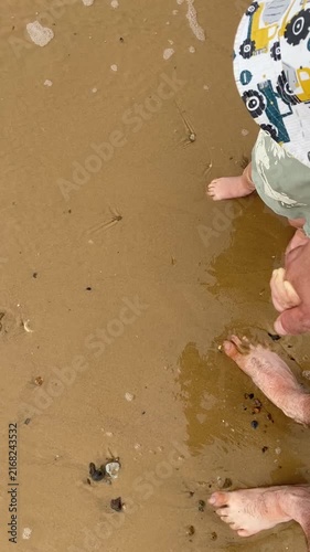 Adult Holding Young Child’s Hand as Waves Wash Over Their Feet