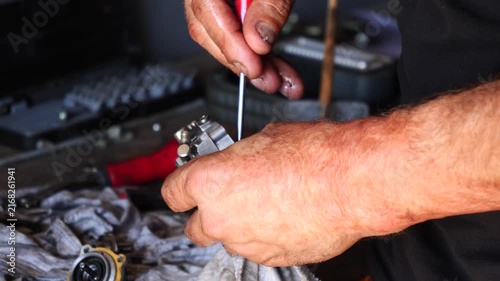 Close-up of mechanic's weathered hands repairing a mechanical part with a screwdriver.