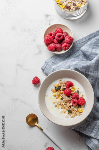Diet low-fat yogurt with muesli, raspberries and honey in a bowl on a marble background