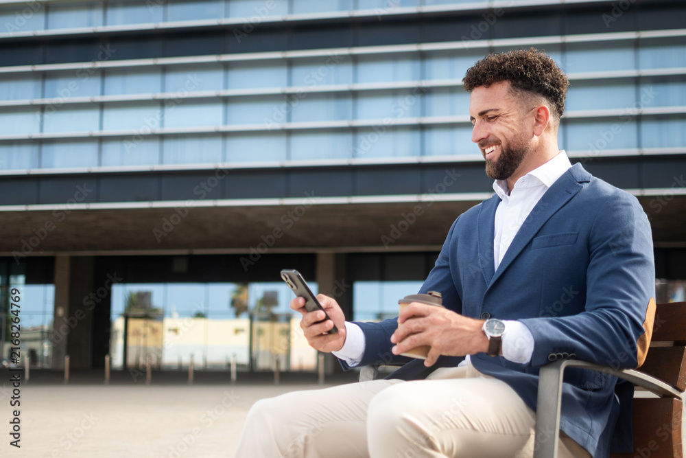 Fototapeta premium Businessman using smartphone while having coffee outside office