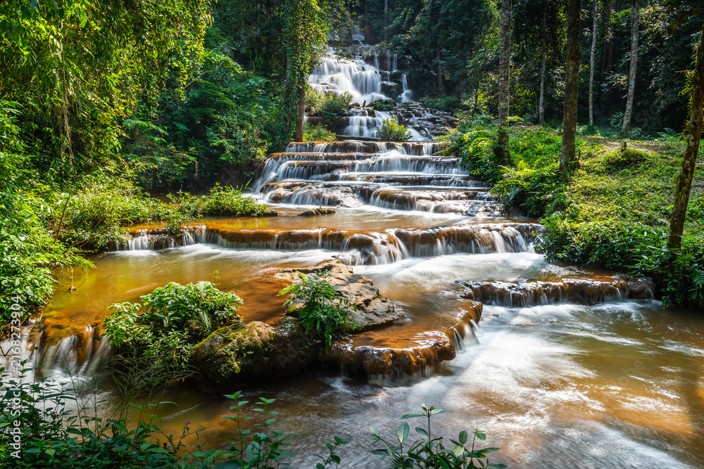 Fototapeta premium Beautiful multi-tiered Pha Charoen Waterfall cascading through lush green tropical rainforest in Namtok Pha Charoen National Park, Phop Phra District, Tak Province, Thailand.