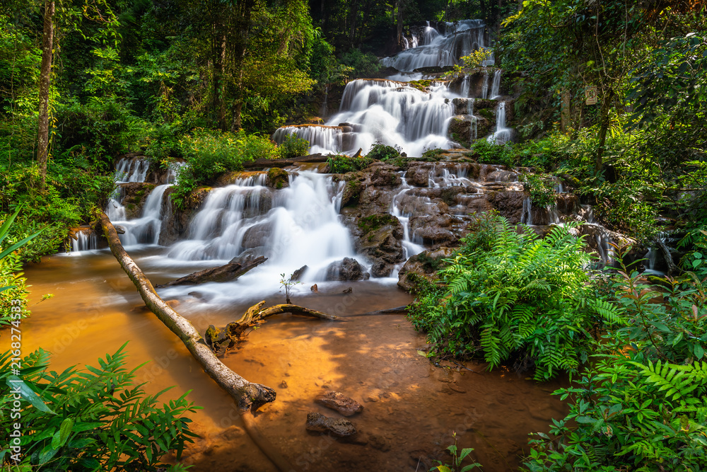 Obraz premium Beautiful multi-tiered Pha Charoen Waterfall flowing through a lush tropical rainforest stream in Namtok Pha Charoen National Park, Phop Phra District, Tak Province, Thailand.