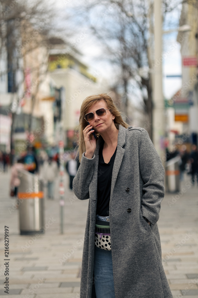 Fototapeta premium Woman talking on phone walking urban street