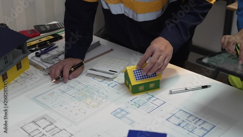 A close-up shot of an architect and a civil engineer discussing blueprints and a house model in an office at night.
