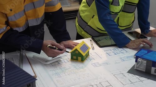 A close-up shot of an architect and a civil engineer discussing blueprints and a house model in an office at night.